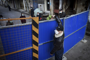 A man in a protective mask passes a container of food over a fence.