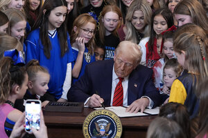 Young girls stand near President Donald Trump (seated), watching as he signs a ban on transgender competitors in women's or girls' sports.