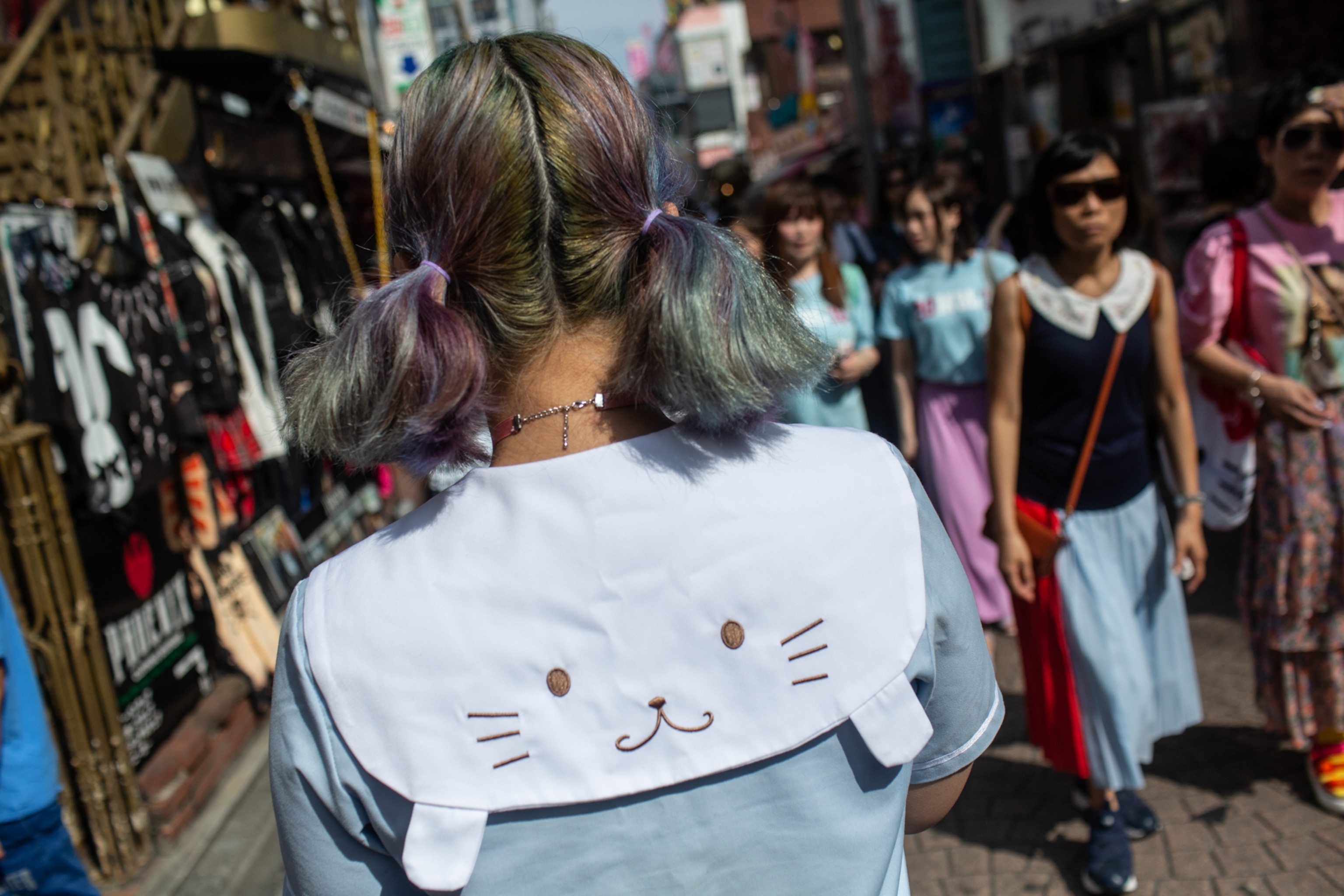 A person with pigtails and a hoodie walk on a crowded street.