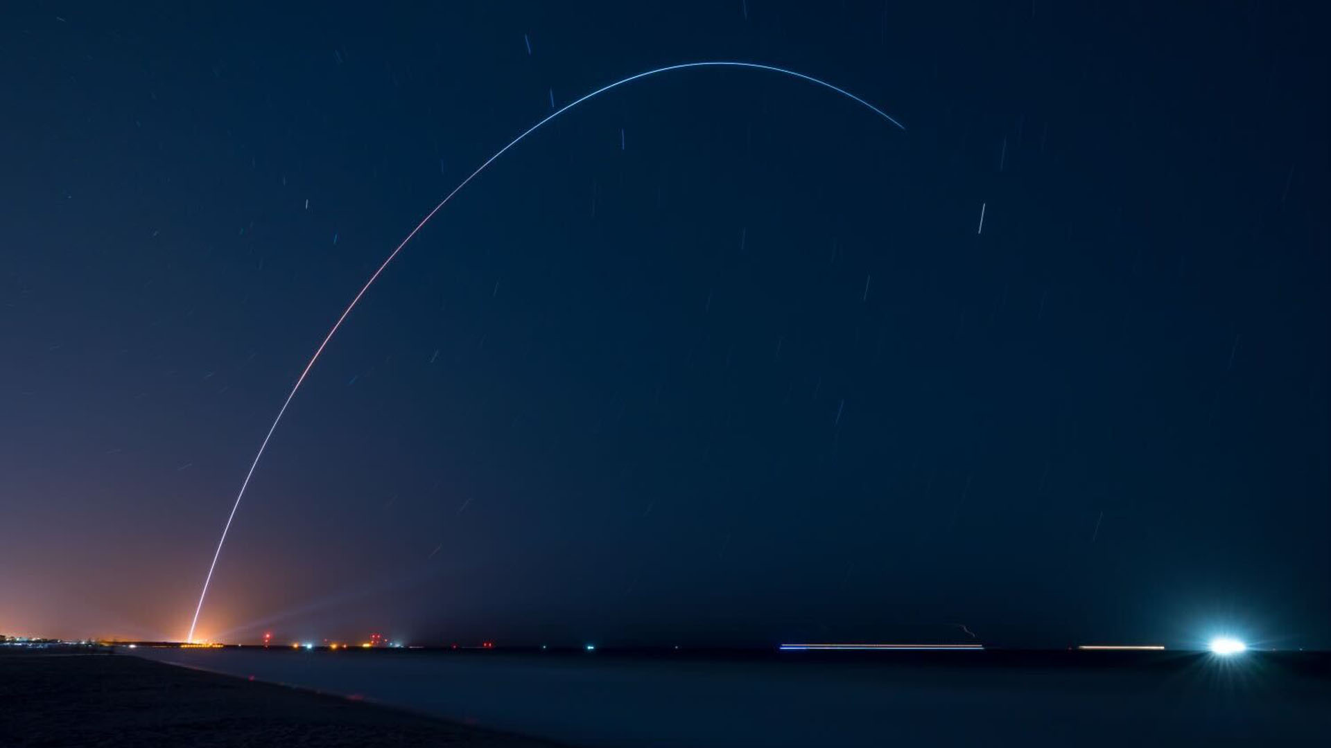 long-exposure photo of a rocket launch at night, showing the vehicle's path through the dark skies as a curving yellowish streak