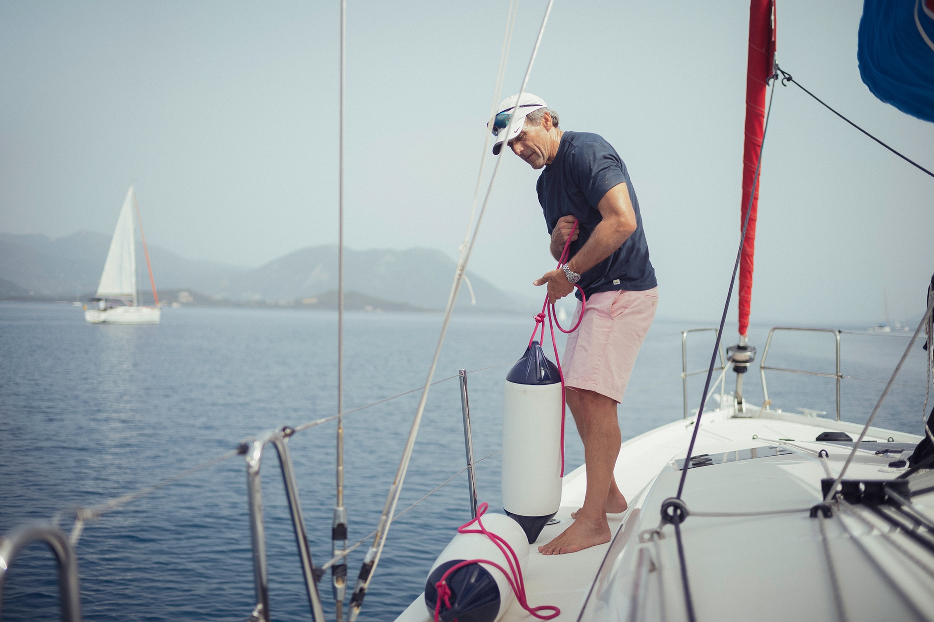 A 60-year-old, fit Greek man pulling boat bumpers on deck of his sailing boat.