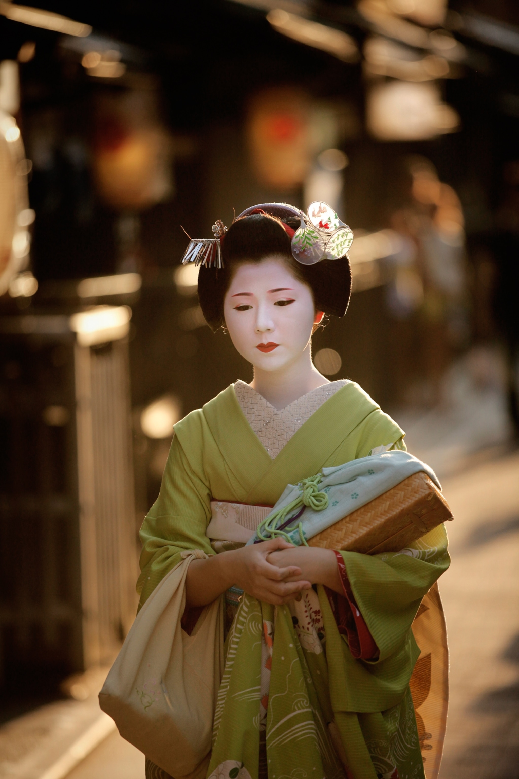A woman with white face paint green Kimono is photographed in warm light.