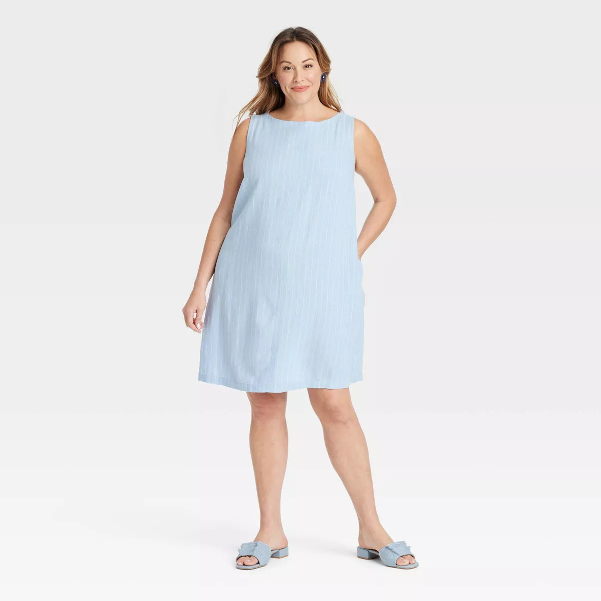 Person wearing a sleeveless, knee-length linen dress with flat sandals, standing in a relaxed pose