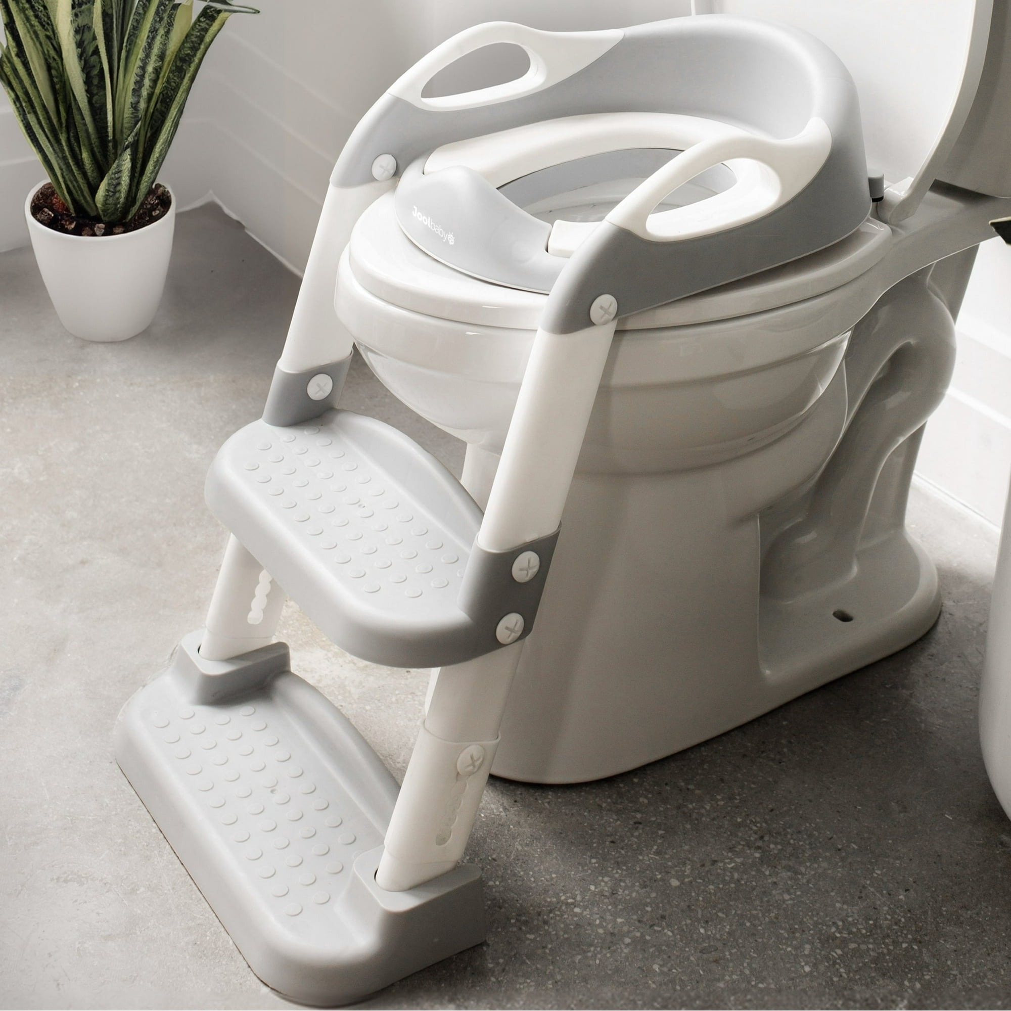 Child toilet training seat with steps, designed for easy access and safety. A potted plant is in the background