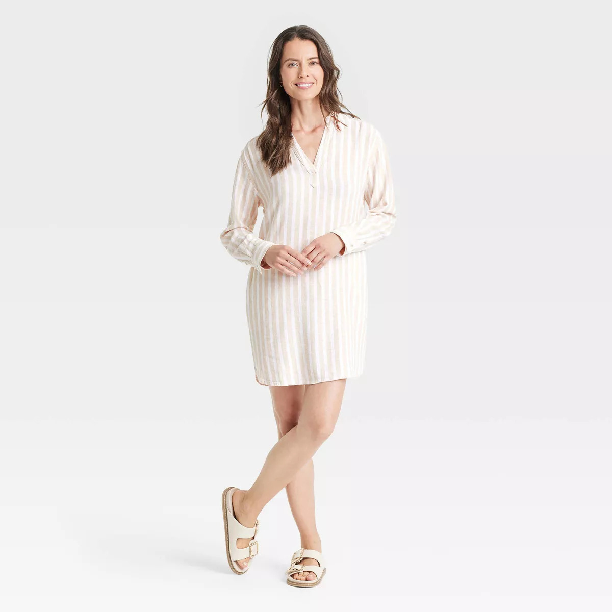Woman in a striped, long-sleeve shirt dress and sandals posing with a smile