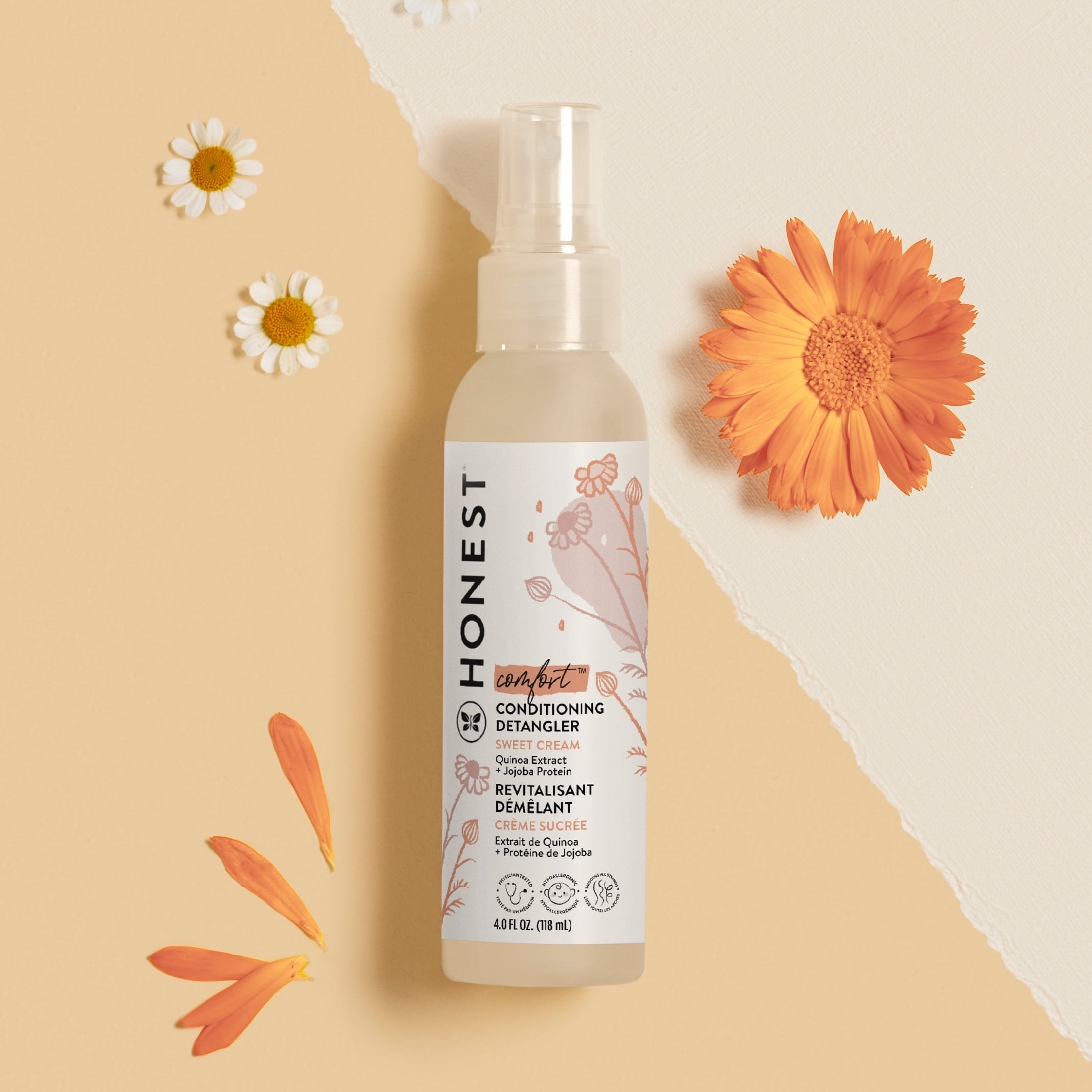 Honest Company Conditioning Detangler bottle with floral design, surrounded by orange and white daisy-like flowers, on a neutral background