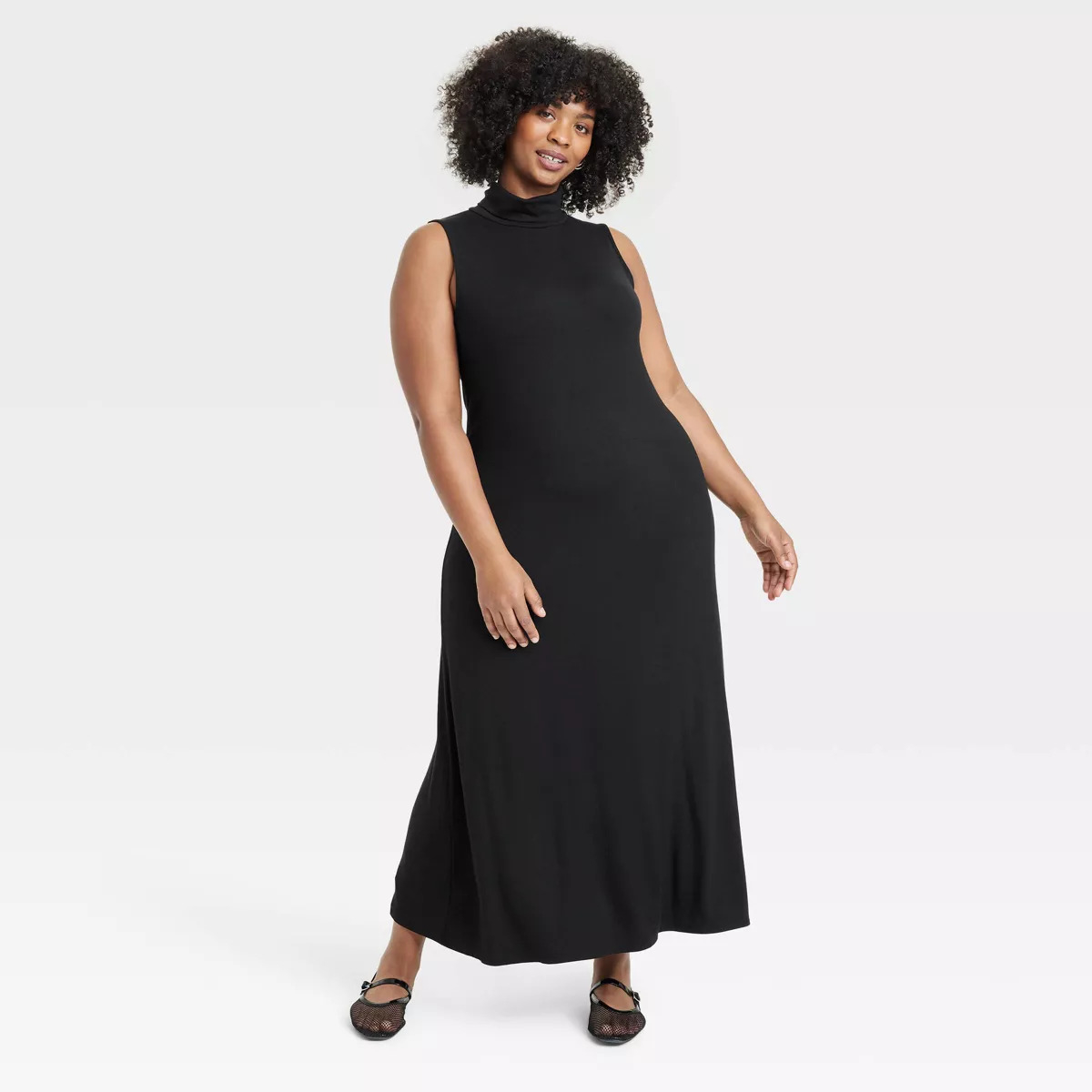 Person in sleeveless, ankle-length dress, smiling, with curly hair. The look is casual and suitable for everyday or semi-formal occasions