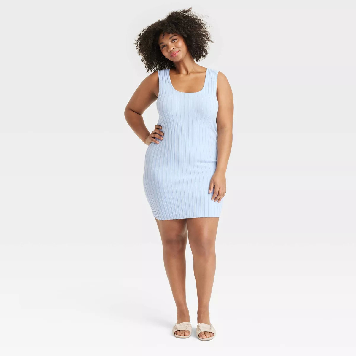 Person wearing a sleeveless, fitted, ribbed dress with open-toe sandals, posing confidently