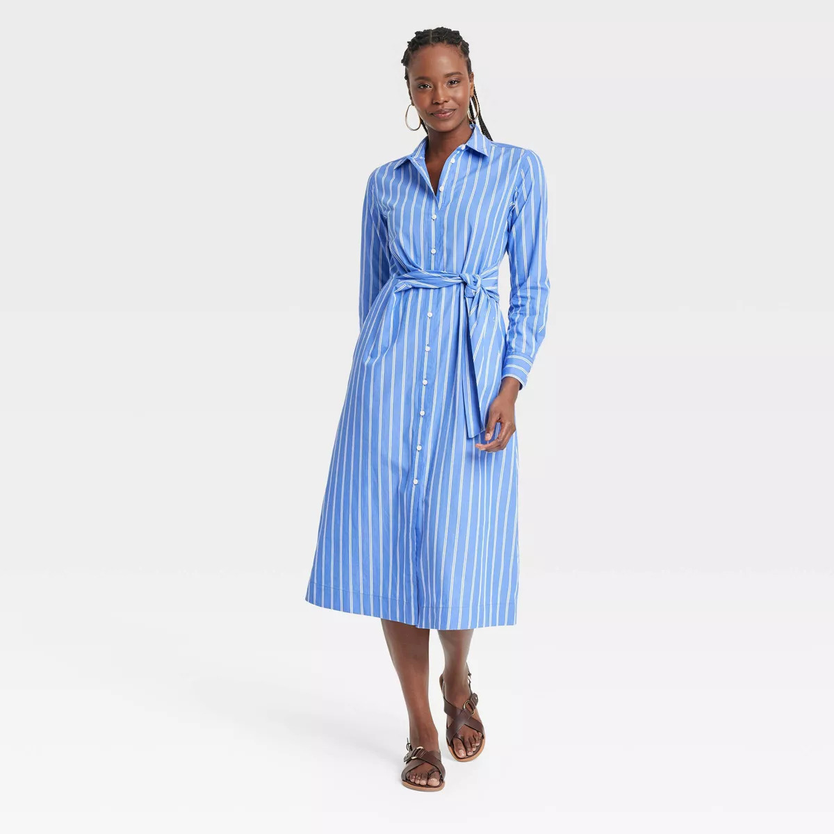 Person wearing a button-up, striped midi dress with a waist tie and sandals, posing for a shopping article