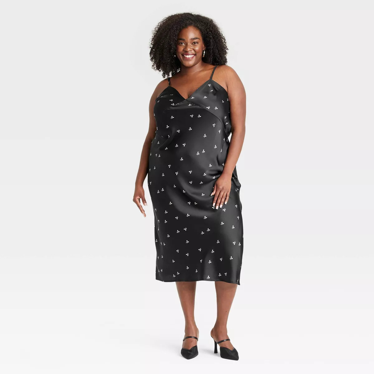 A person wearing a stylish satin slip dress with a delicate pattern, paired with heels, poses confidently