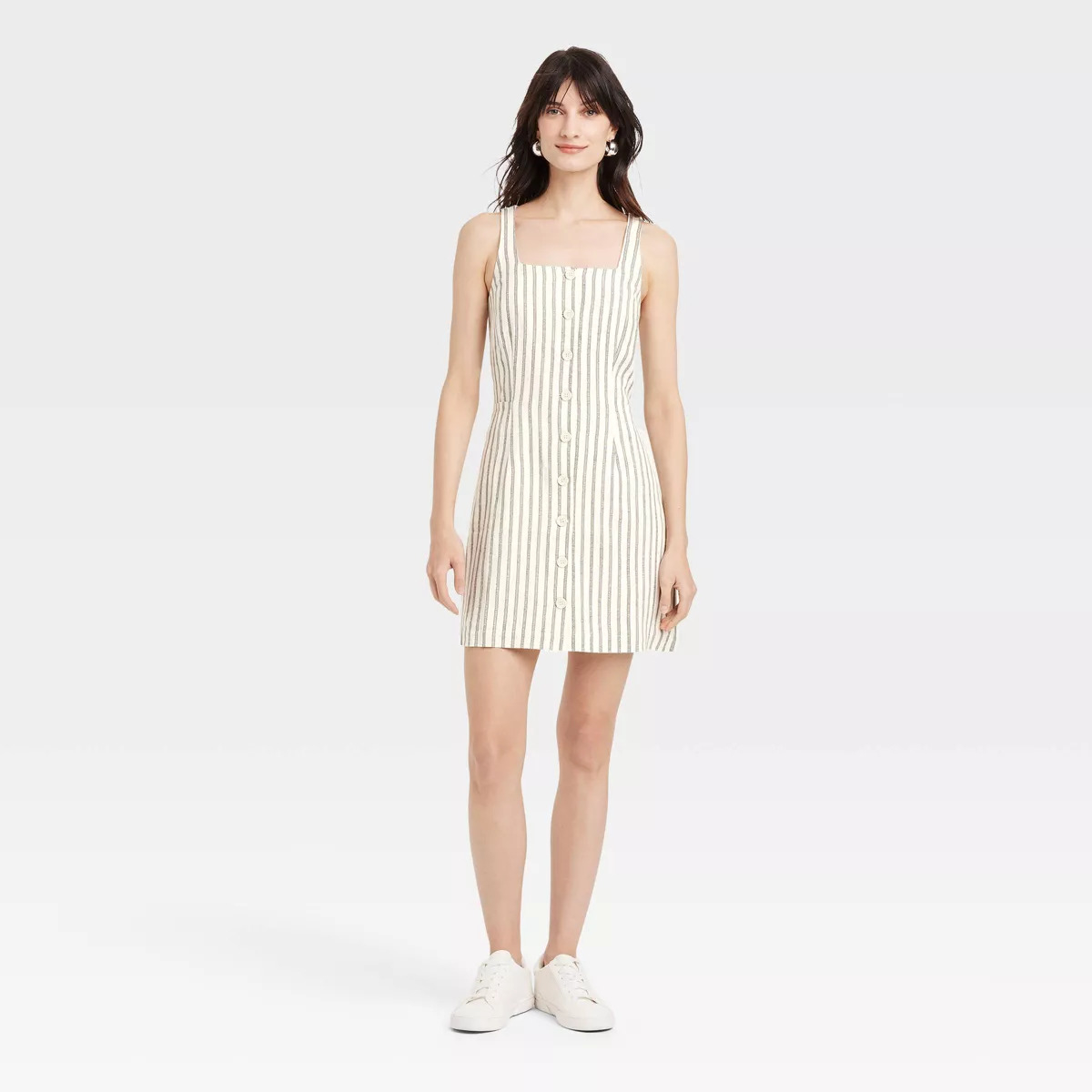 Woman in a striped button-down summer dress and sneakers, standing against a plain background