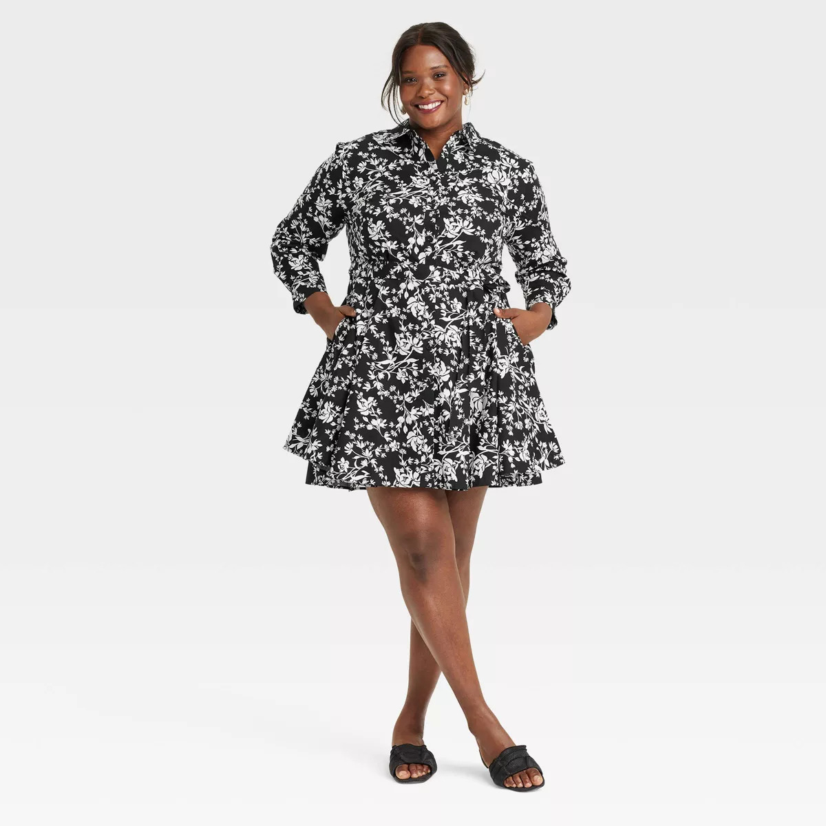 Person modeling a floral-patterned, belted shirt dress with long sleeves and a flared skirt, paired with slip-on sandals