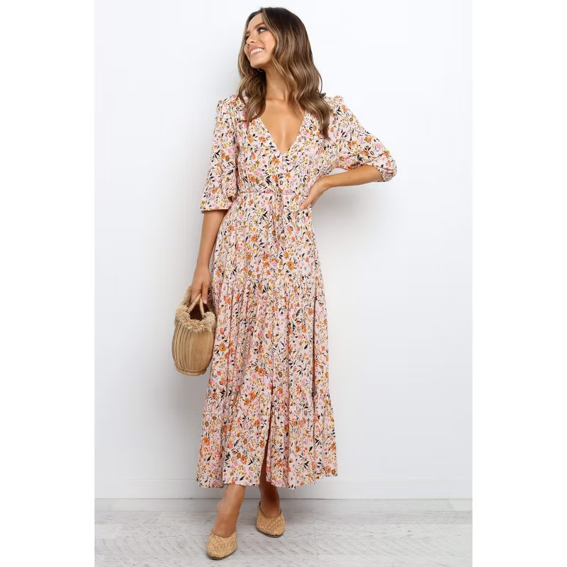 Person in floral maxi dress with puff sleeves, holding a woven bag, stands smiling. Suitable for shopping or spring styling article