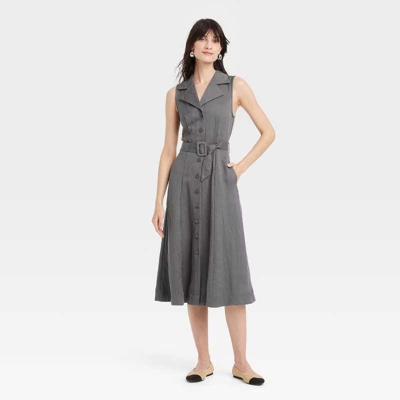 Model wearing a sleeveless, belted button-down dress with a notched collar and midi length, paired with flats. Ideal for casual shopping or outings
