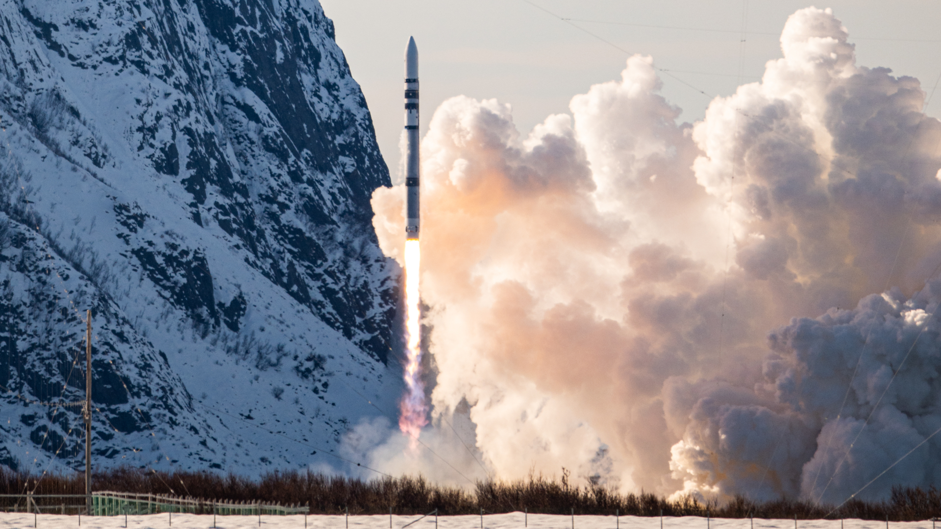 a black and white rocket launching in front of snowy mountains with exhaust plumes