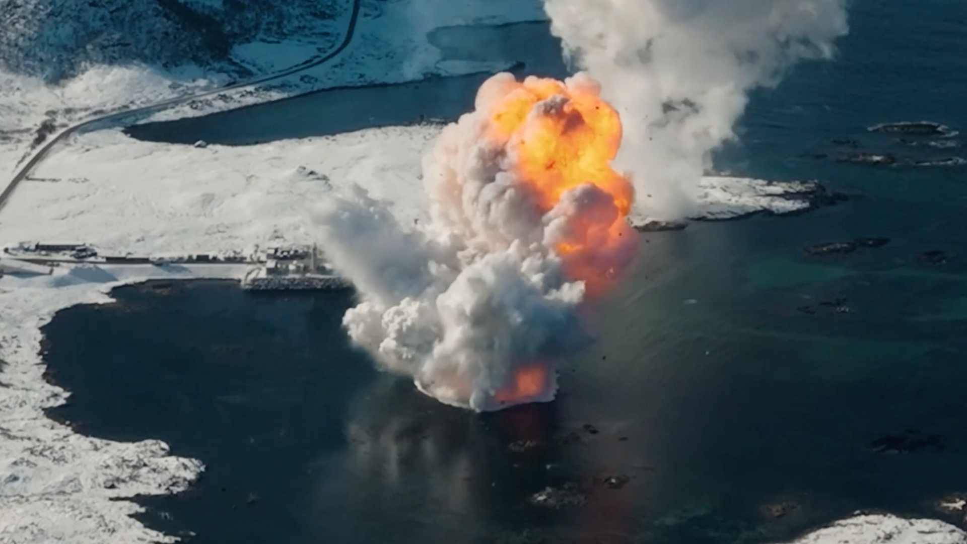 aerial view of an orange-tinted mushroom cloud rising from a sea surrounded by icy mountains