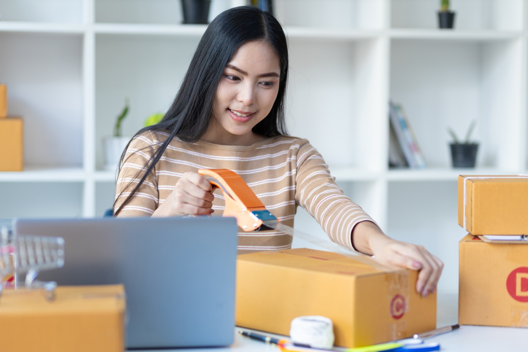 Small start-up business woman working with parcel boxes packing goods in preparation for delivery.