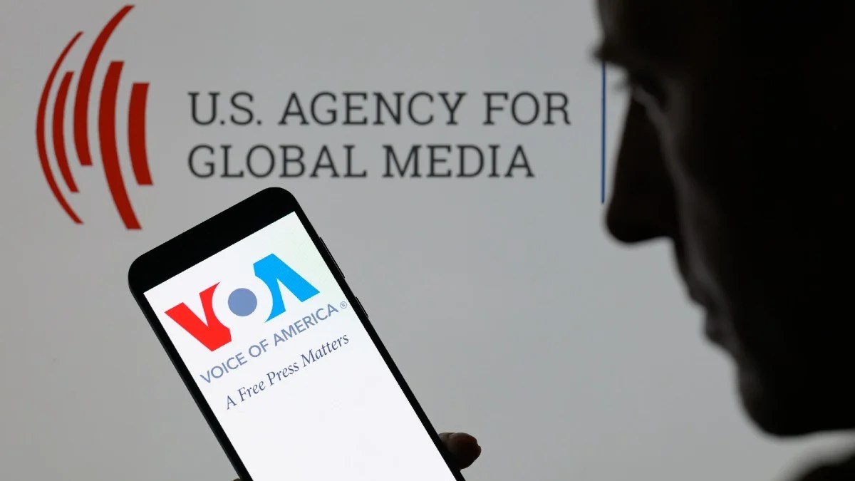 The Voice Of America (VOA) logo on a mobile phone with the US Agency For Global Media logo in background