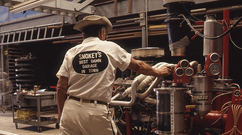 Smokey Yunick in white shirt leaning on an engine