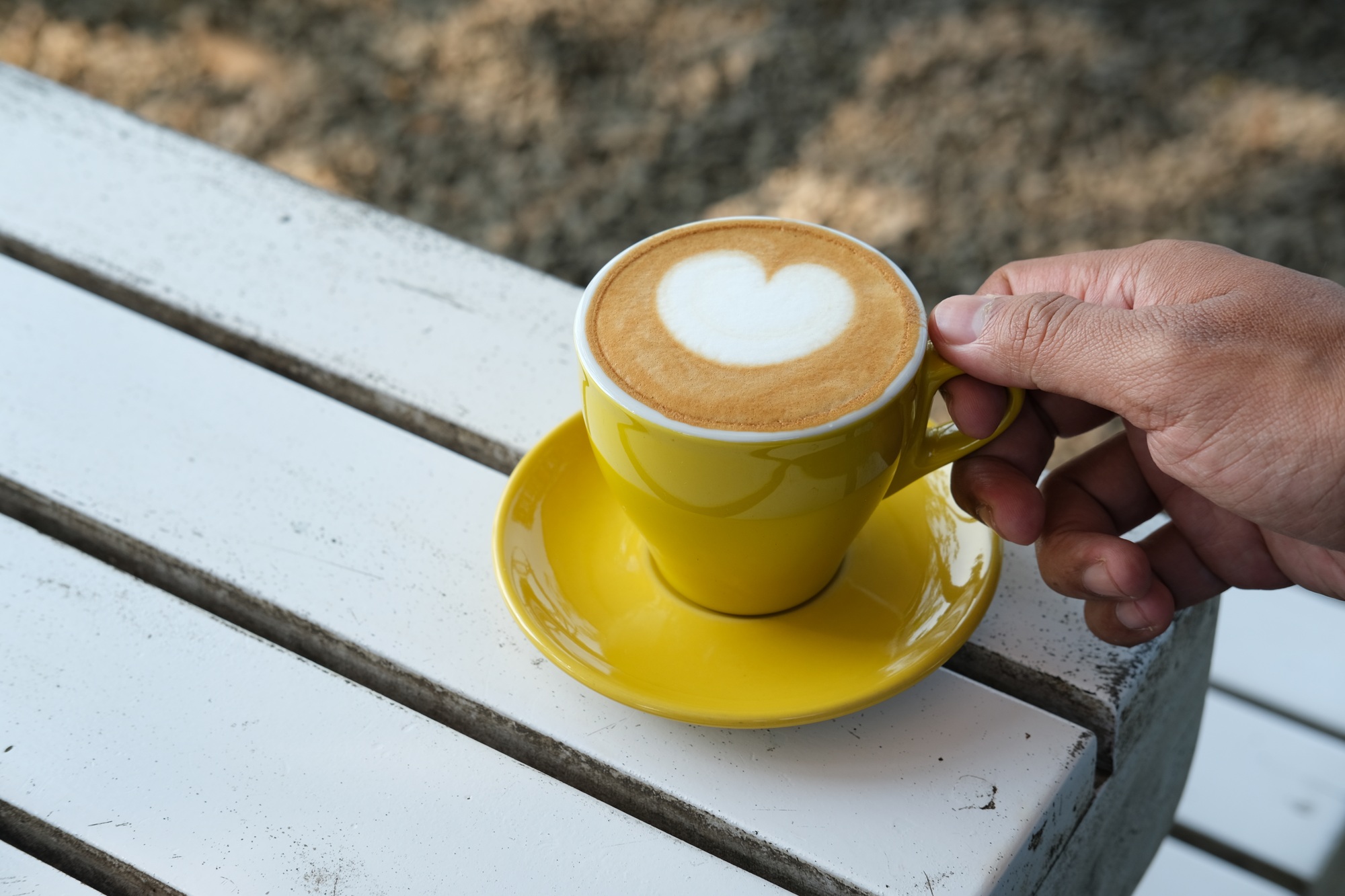 A close-up of a hand holding a yellow cup of coffee with a heart-shaped latte art