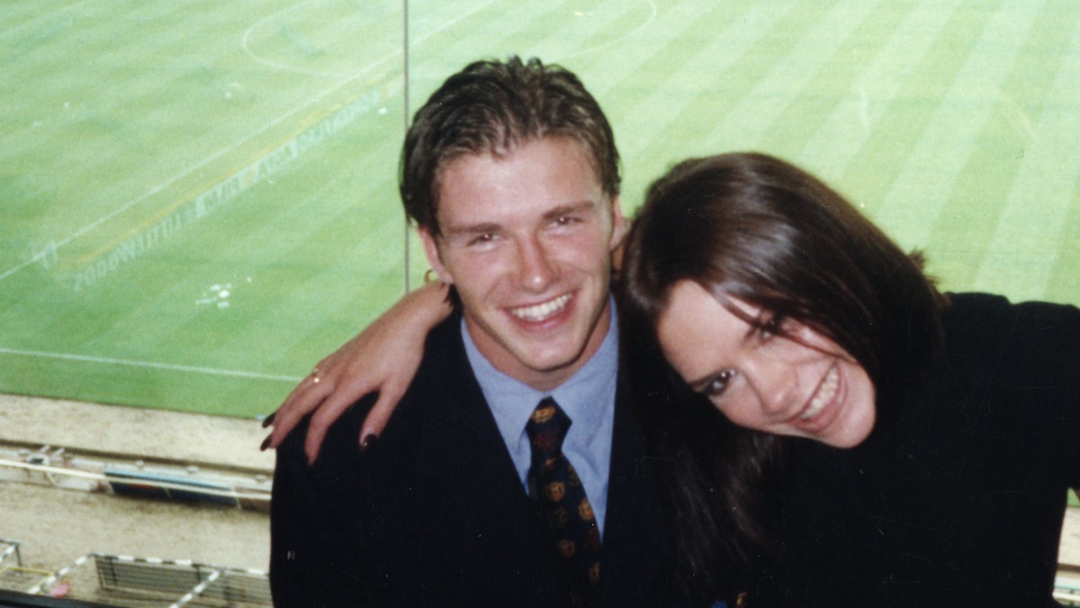 Victoria Beckham in a black coat, David Beckham in a black blazer, blue shirt and tie.