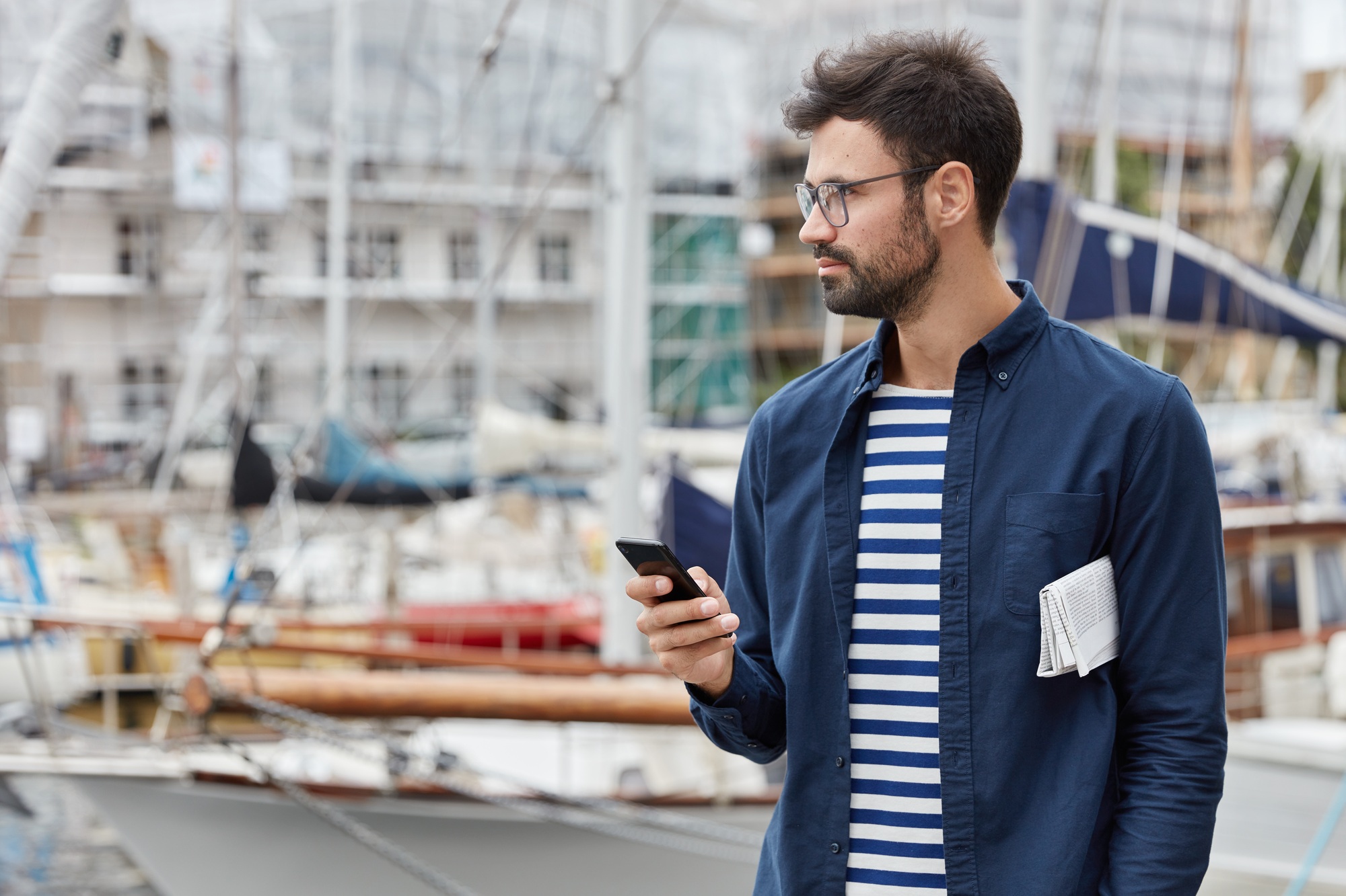 Horizontal view of thoughtful freelancer blogs in social networks, holds contemporary mobile phone,