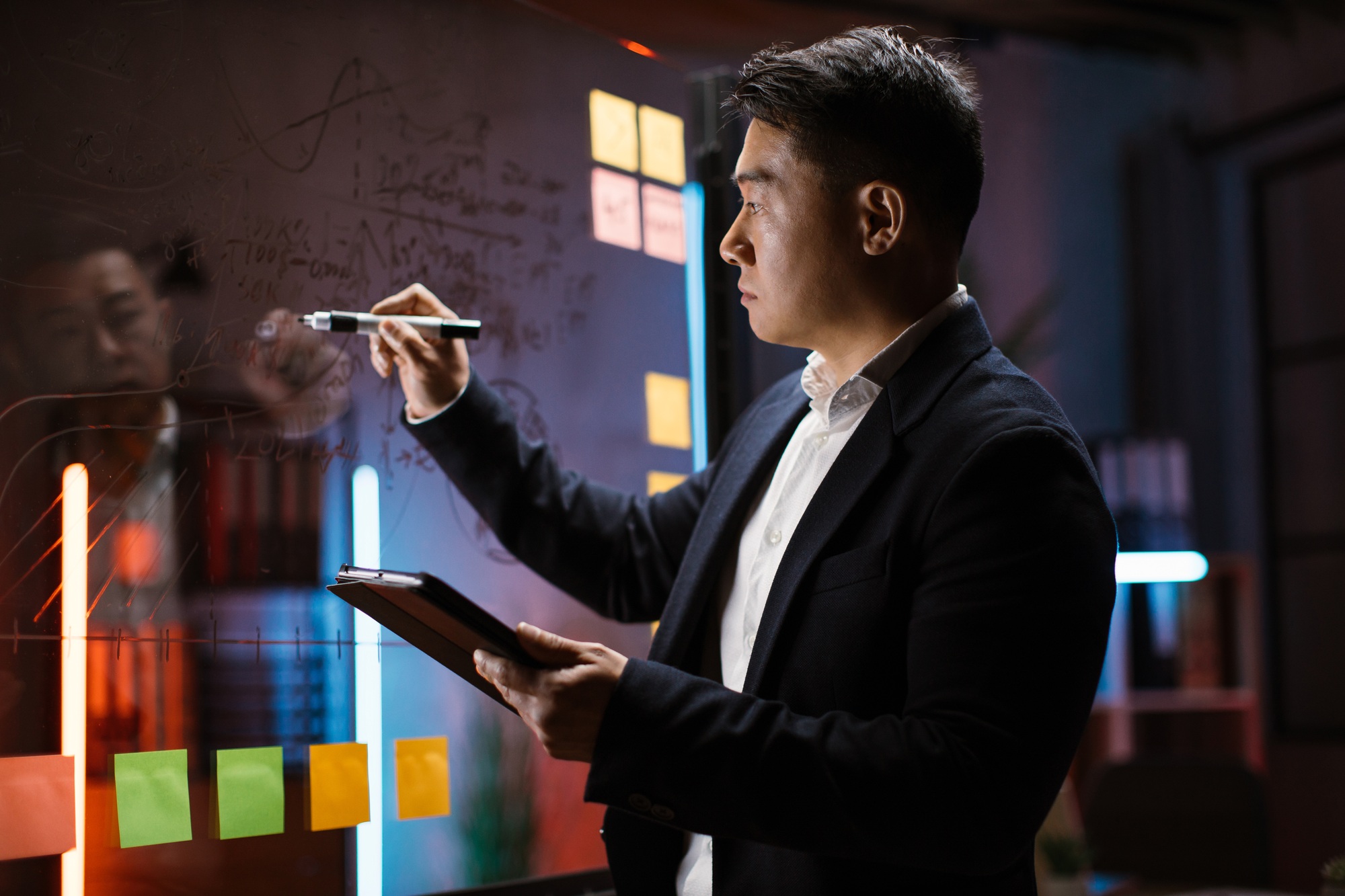Male Asian employee writing on glass wall, developing business project at workplace