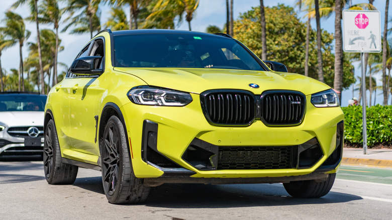 a yellow BMW car driving on a street with palm trees