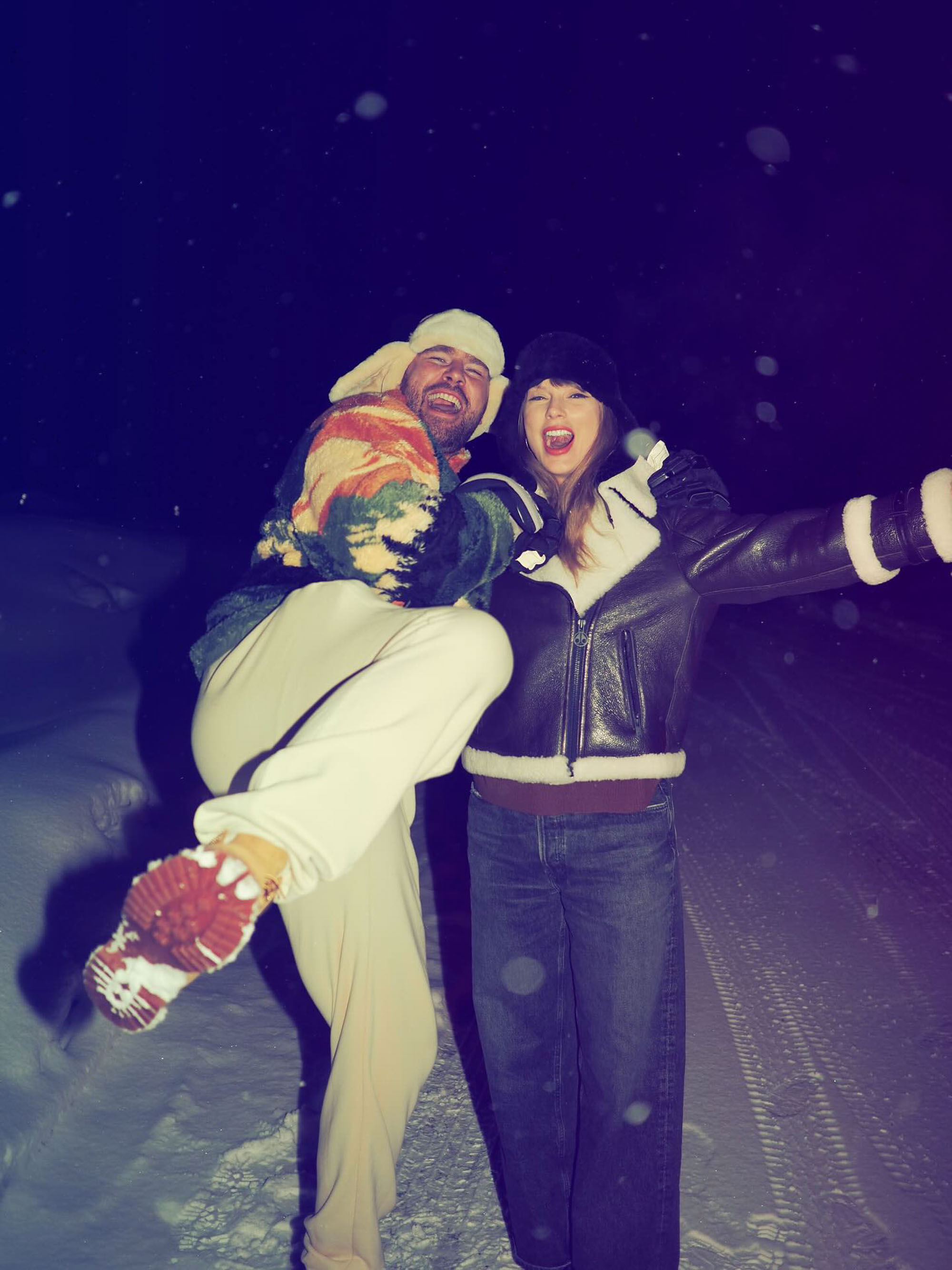 Travis Kelce holding Taylor Swift in a snowy, outdoor setting at night.