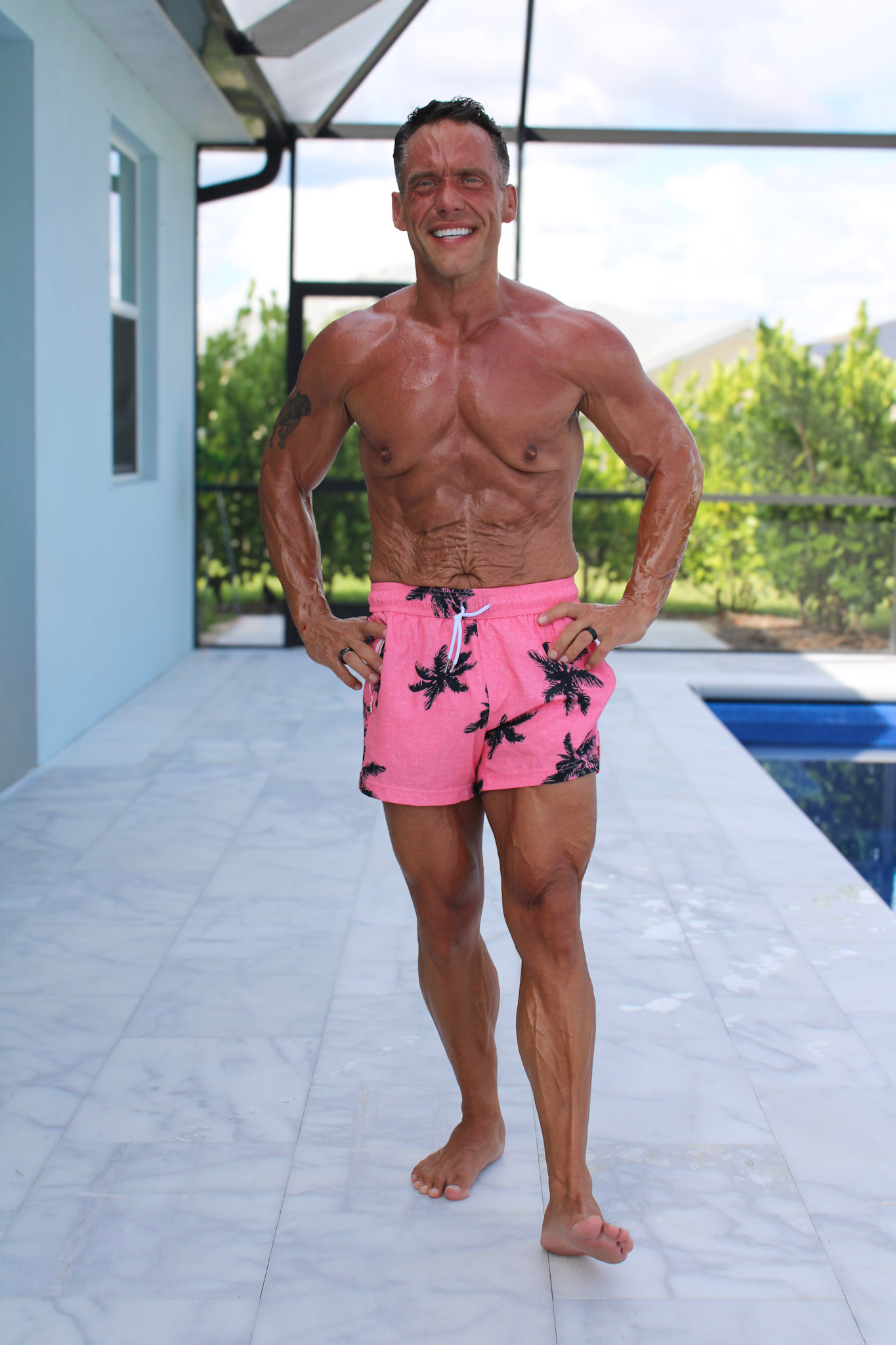 fit shirtless man standing by a pool in a swimsuit