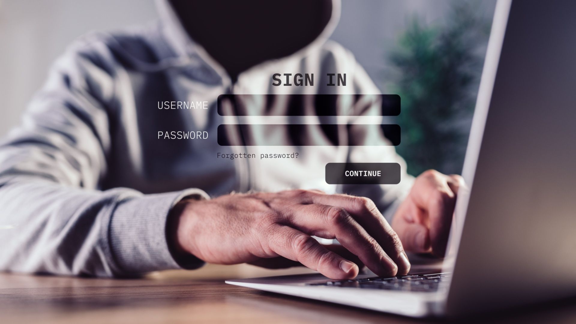 A dark hooded figure ominously using a laptop.