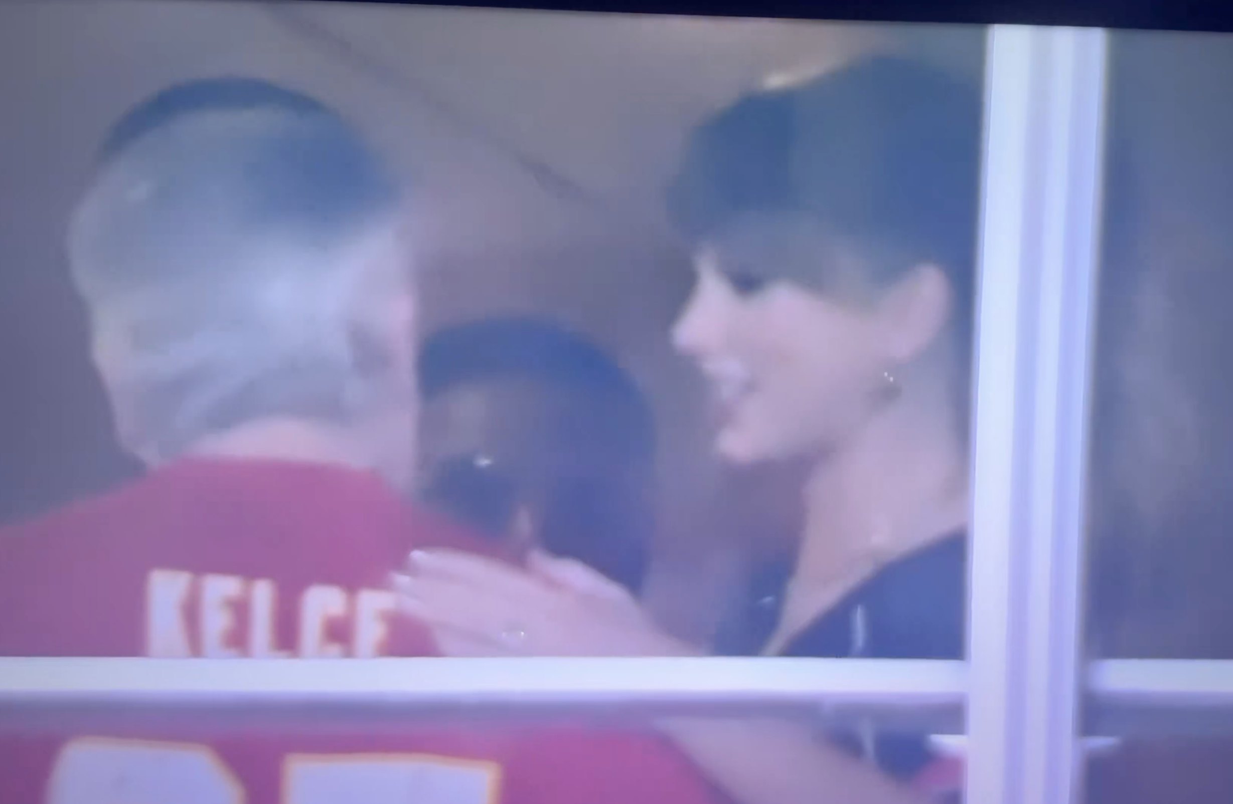 Taylor Swift smiles while speaking to a person wearing a red jersey with 
