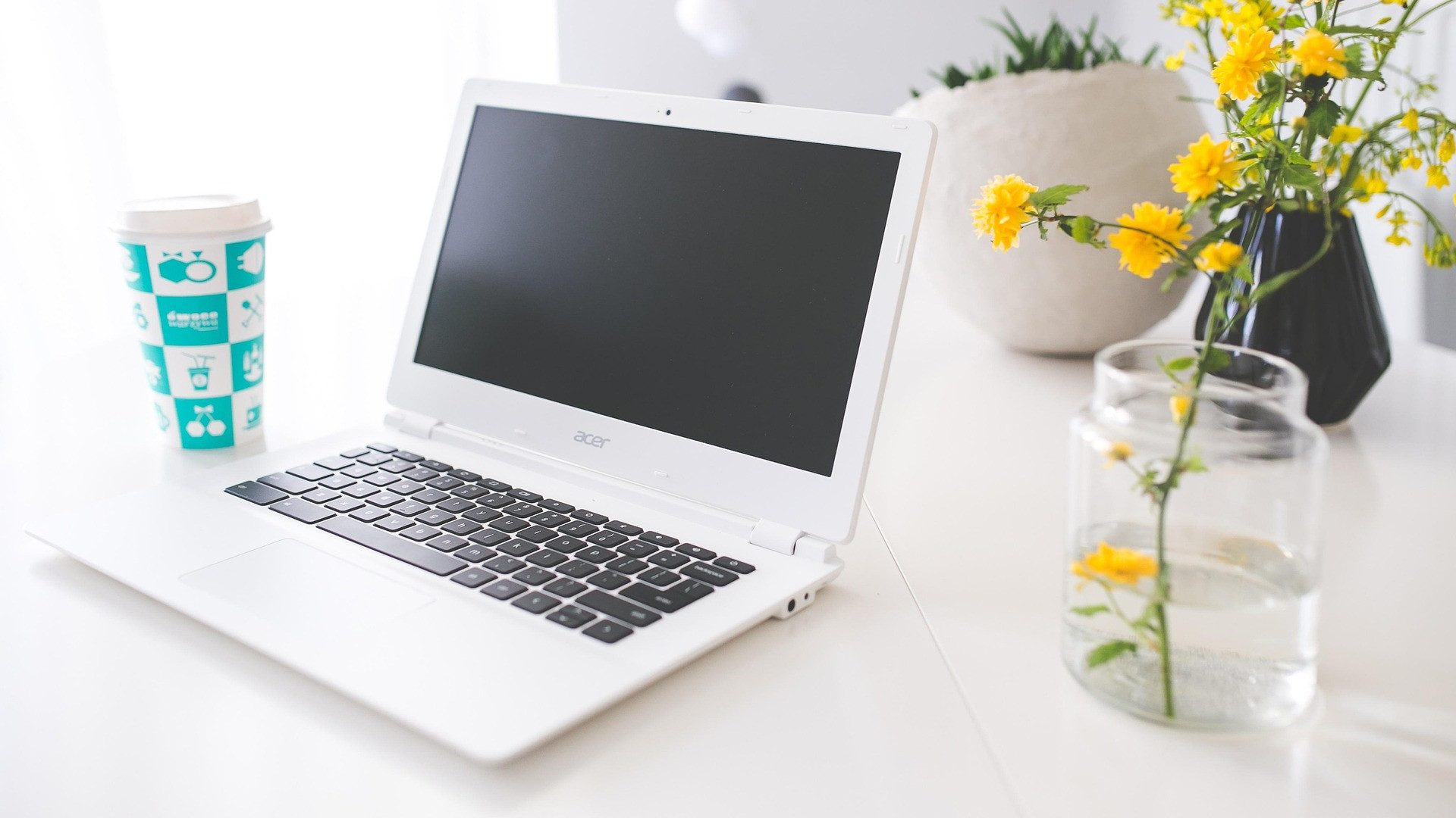 Acer Chromebook on white desk with flower in vase beside it