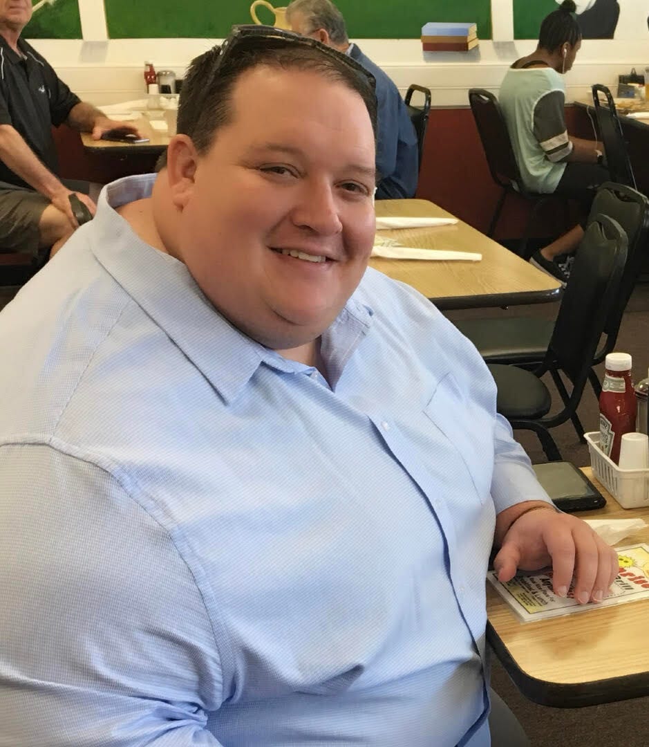 obese man smiling as he sits on a table in a busy restaurant